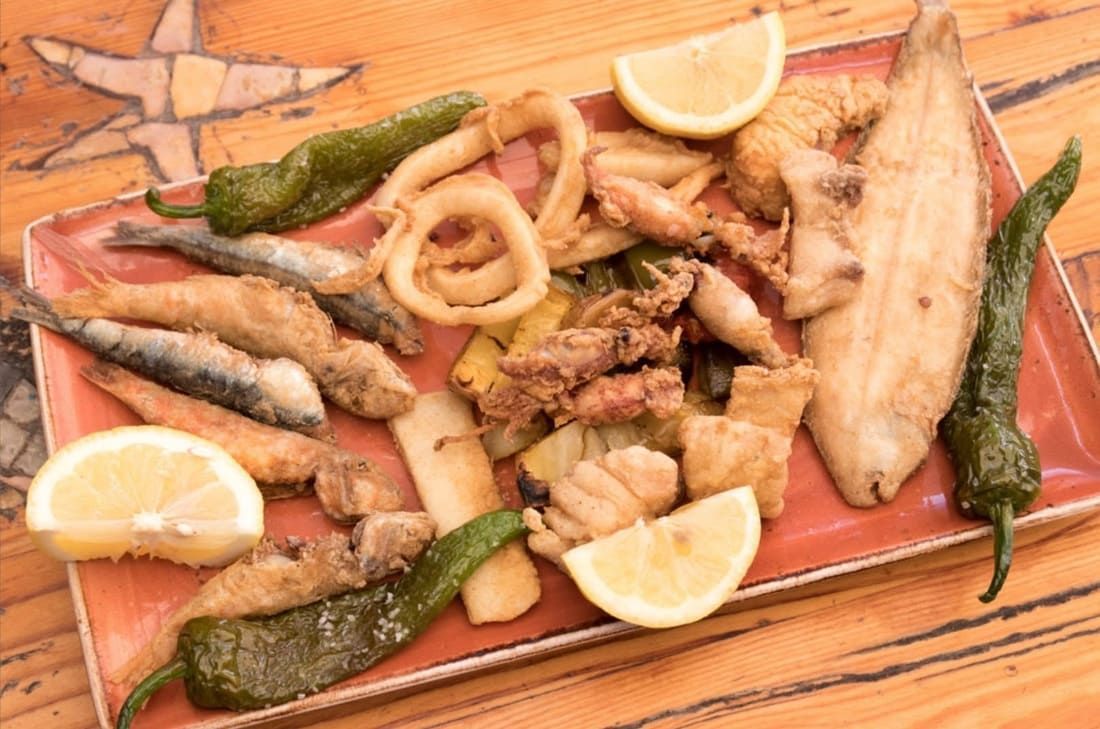 Surtido de mariscos y verduras fritas en una fuente de madera con rodajas de limón.