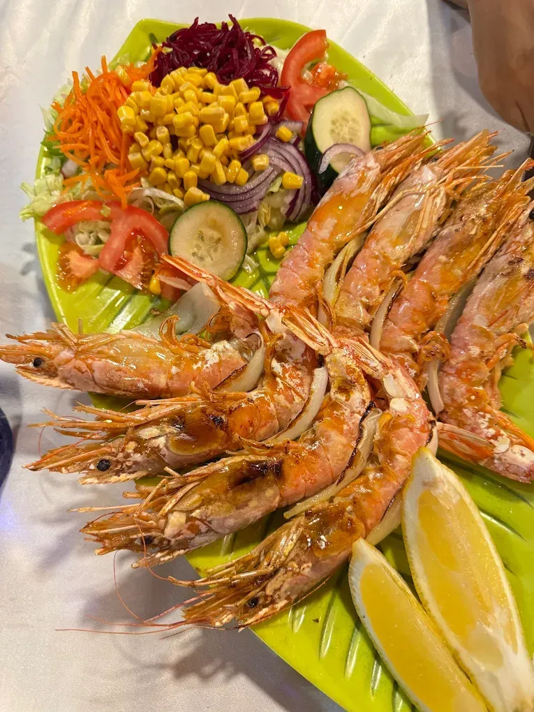 Camarones a la parrilla con ensalada y rodajas de limón en un plato verde.