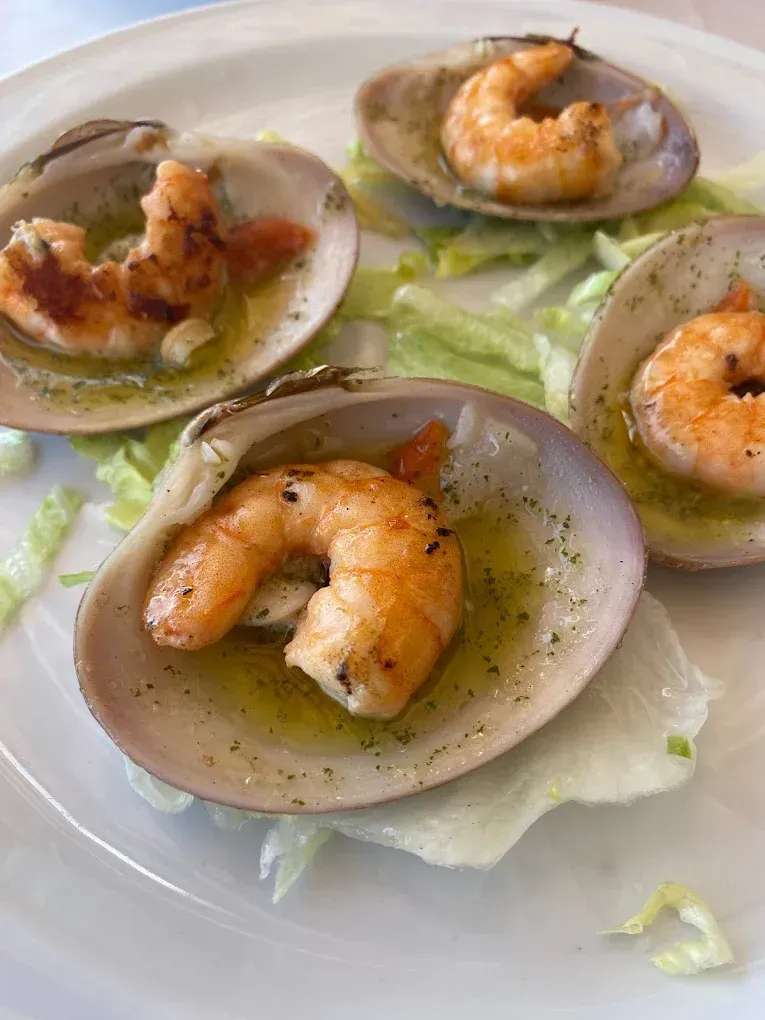 Cuatro camarones cocidos con cáscara sobre lechuga, rociados con aceite.