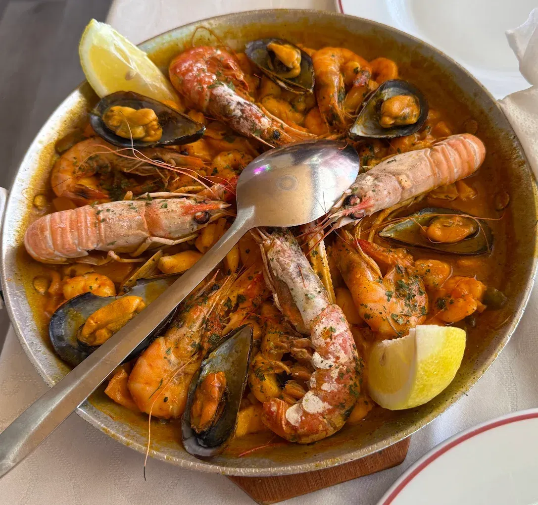Paella de mariscos en sartén metálica, con camarones, mejillones y gajos de limón; una cuchara reposa en el centro.