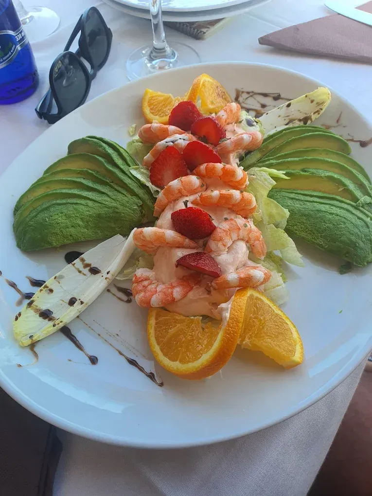 Ensalada de camarones con aguacate, rodajas de naranja y fresas en un plato blanco.