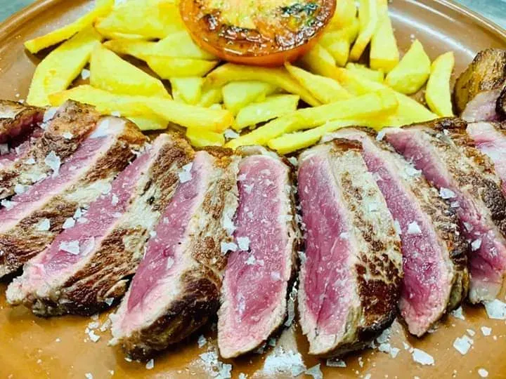 Filete rebanado con papas fritas y tomate, aderezado con sal.