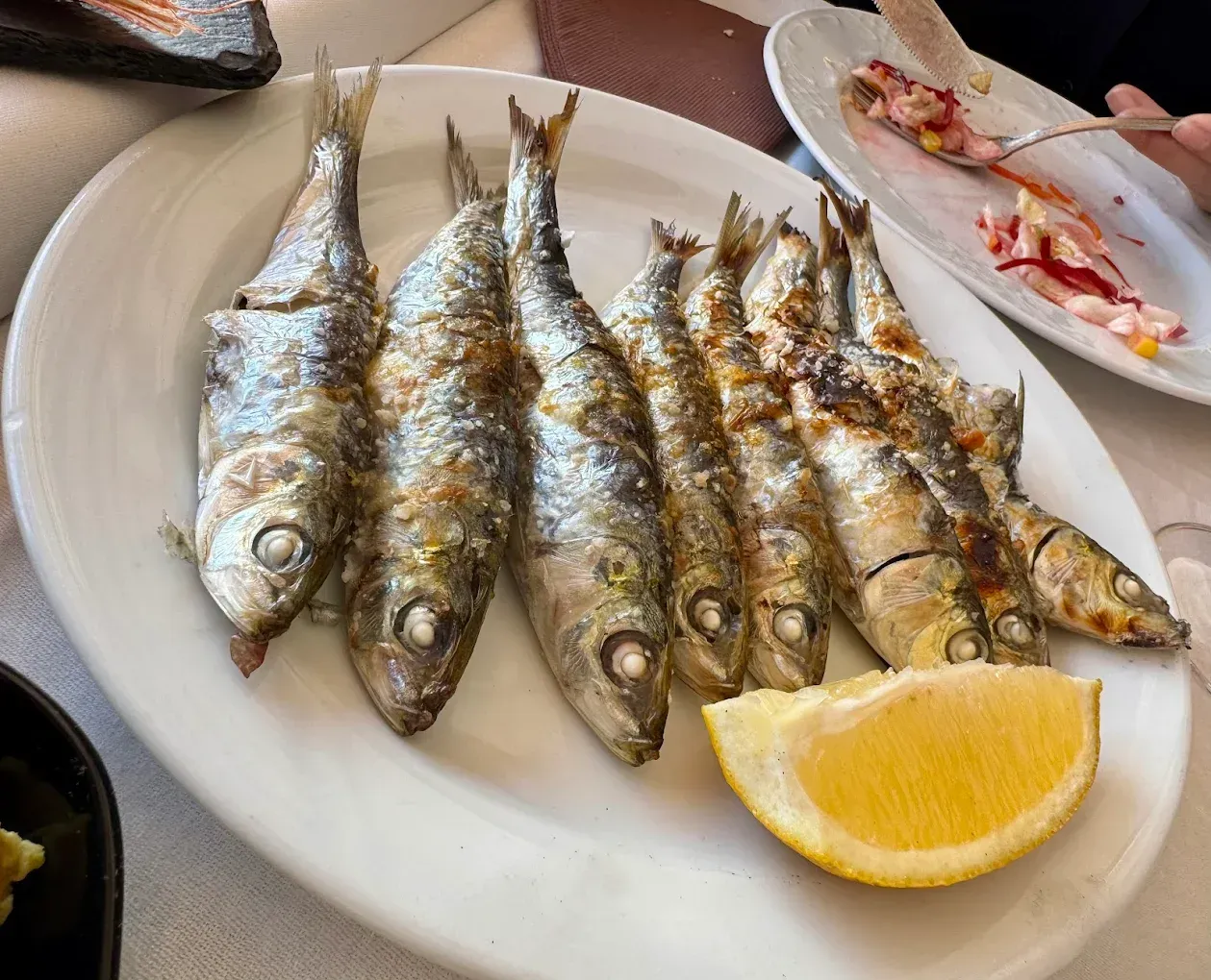 Sardinas a la parrilla en un plato blanco con una rodaja de limón.