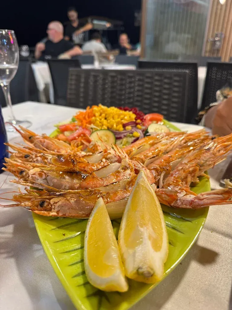 Plato de camarones a la parrilla con rodajas de limón y ensalada en la mesa de un restaurante.