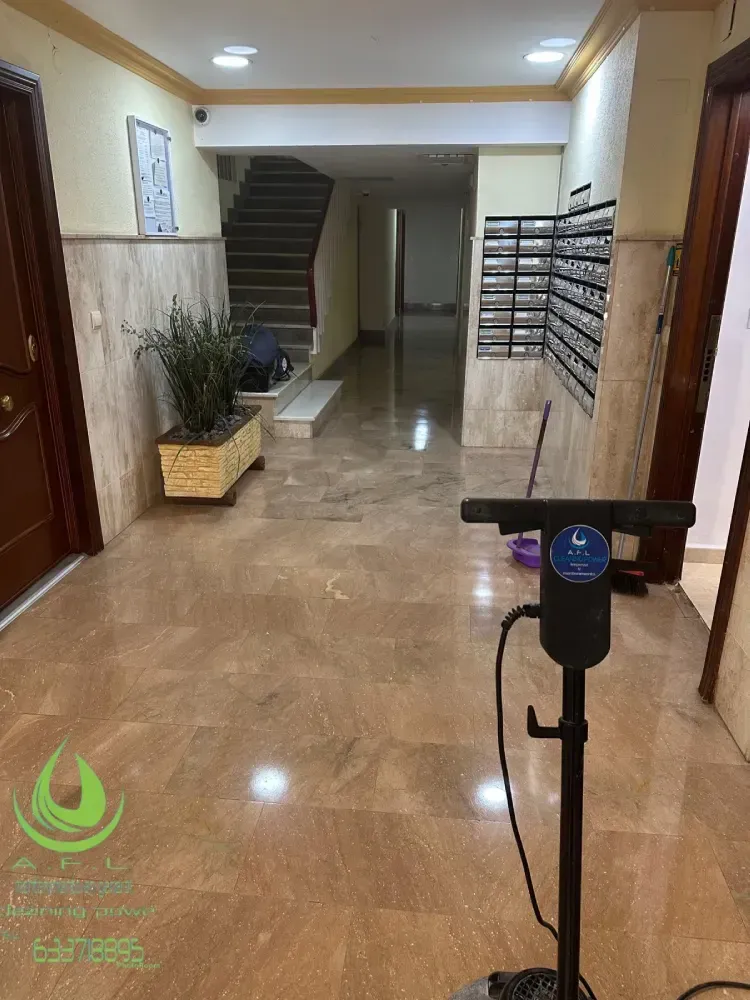 Pasillo con suelos de mármol, escaleras y buzones. Limpiador de suelos en primer plano.