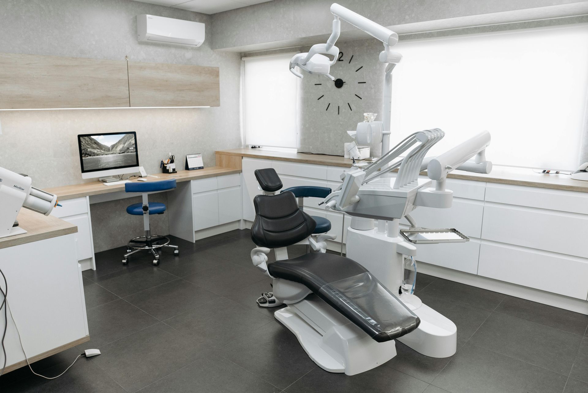 Interior de consultorio dental con sillón y equipo dental. Gabinetes y paredes de color claro, piso oscuro y una ventana.