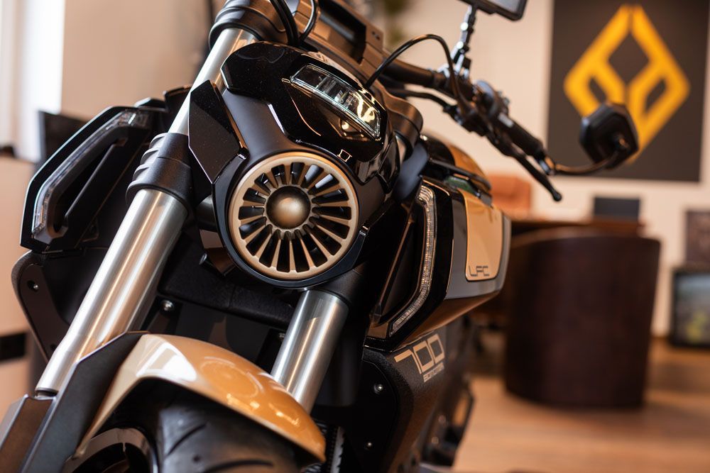 Nahaufnahme eines schwarzen Motorrads in einem Ausstellungsraum, im Hintergrund sind ein verschwommener Tisch und Wanddekoration zu sehen.