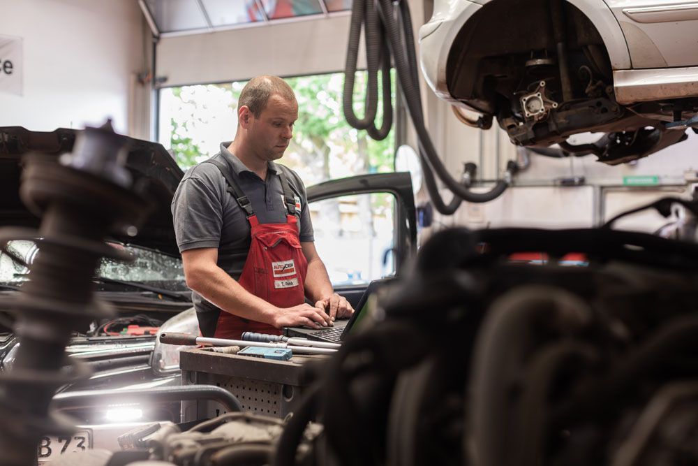Ein Mechaniker in roter Schürze arbeitet in einer Autowerkstatt unter einem Auto.
