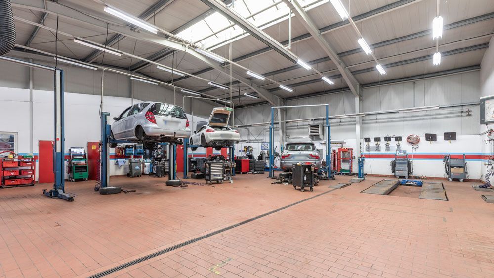 Große Autowerkstatt mit Hebebühnen, Werkzeugen und mehreren Fahrzeugen unter einem hohen Metalldach