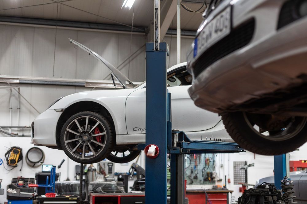 Zwei Autos wurden in einer Autowerkstatt mit hydraulischen Hebebühnen angehoben; Werkzeuge und Ausrüstung befanden sich in der Nähe.