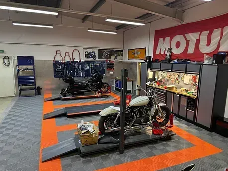 Motorräder werden auf erhöhten Podesten in einem Ausstellungsraum mit orange-blauem Boden präsentiert.