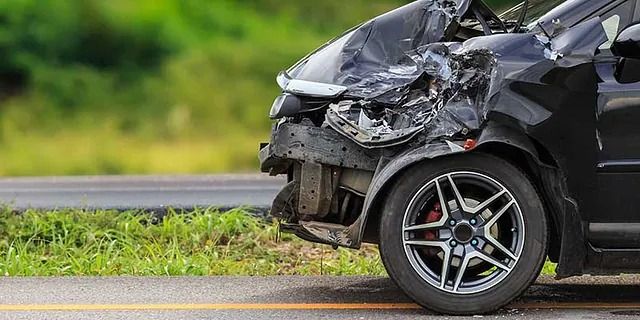 Schwarzer Pkw mit schwerem Frontschaden nach einem Zusammenstoß am Straßenrand auf einem Grünstreifen