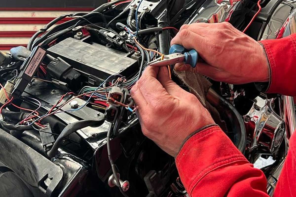 Hände, die mit einem Multimeter verhedderte Kabel im Inneren eines elektronischen Geräts prüfen.