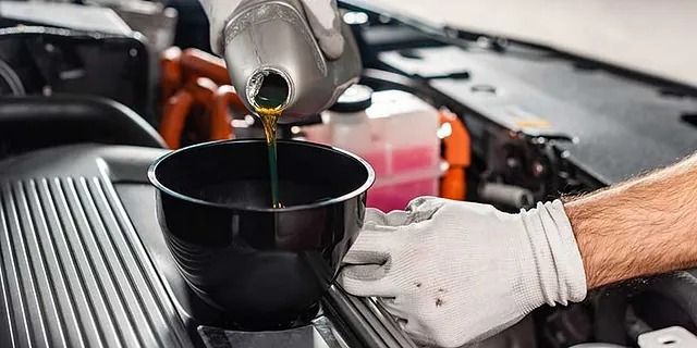 Motoröl wird mit einem Trichter und einer behandschuhten Hand in einen Automotor eingefüllt.