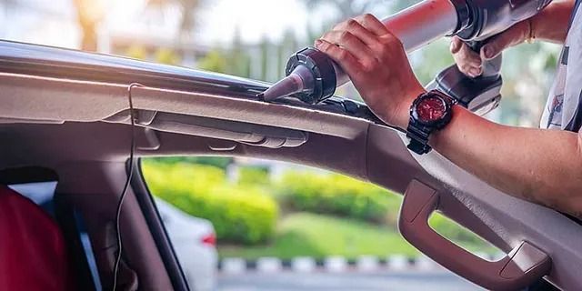 Hände benutzen einen Staubsaugerschlauch, um den Innenraum eines Autos bei geöffnetem Verdeck zu reinigen.