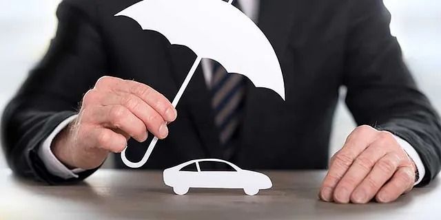 Eine Person hält einen weißen Regenschirm über ein weißes Spielzeugauto auf einer dunklen Oberfläche.