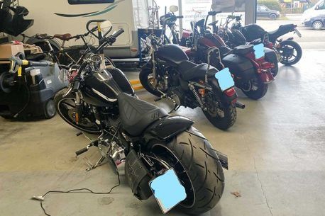 Eine Reihe geparkter Motorräder in einem Ausstellungsraum, im Vordergrund ein schwarzes Chopper-Motorrad.