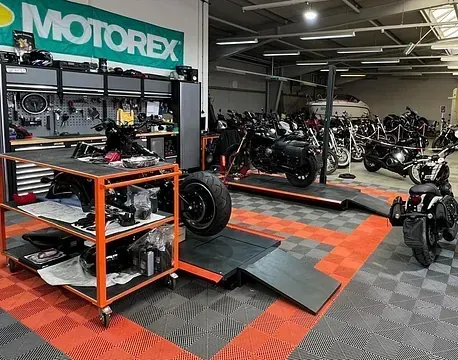 Motorradwerkstatt mit Motorrädern, Werkzeugen und einem Motorex-Schild in einem schwarz-orangenen Servicebereich