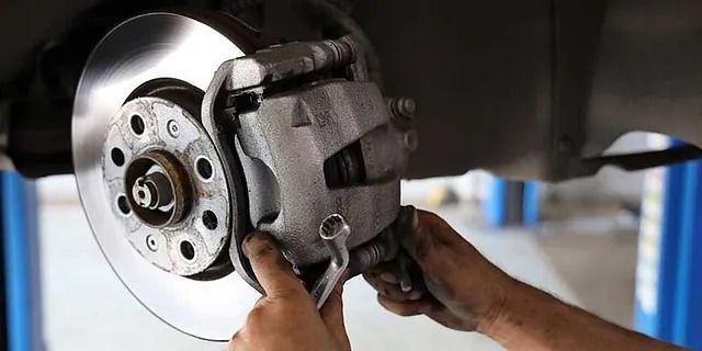 Ein Mechaniker montiert einen Bremssattel an einem Autorad; im Hintergrund ist ein angehobenes Fahrzeug zu sehen.