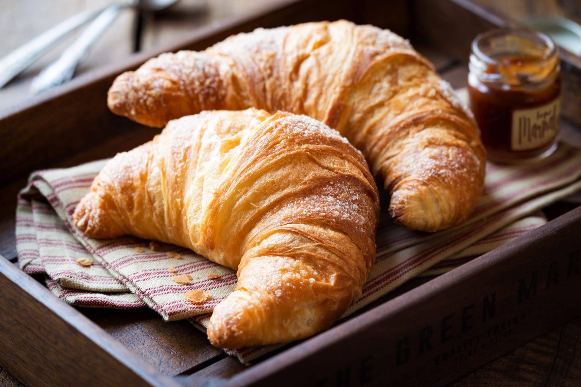 Zwei Croissants liegen auf einem Holztablett neben einem Glas Marmelade.