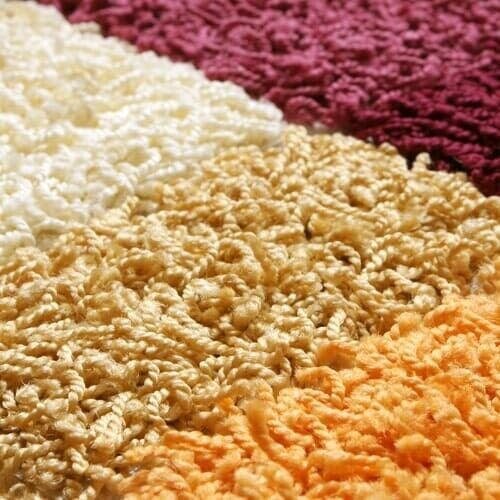 Close-up de um tapete colorido e texturizado com seções em branco, dourado, laranja e bordô.