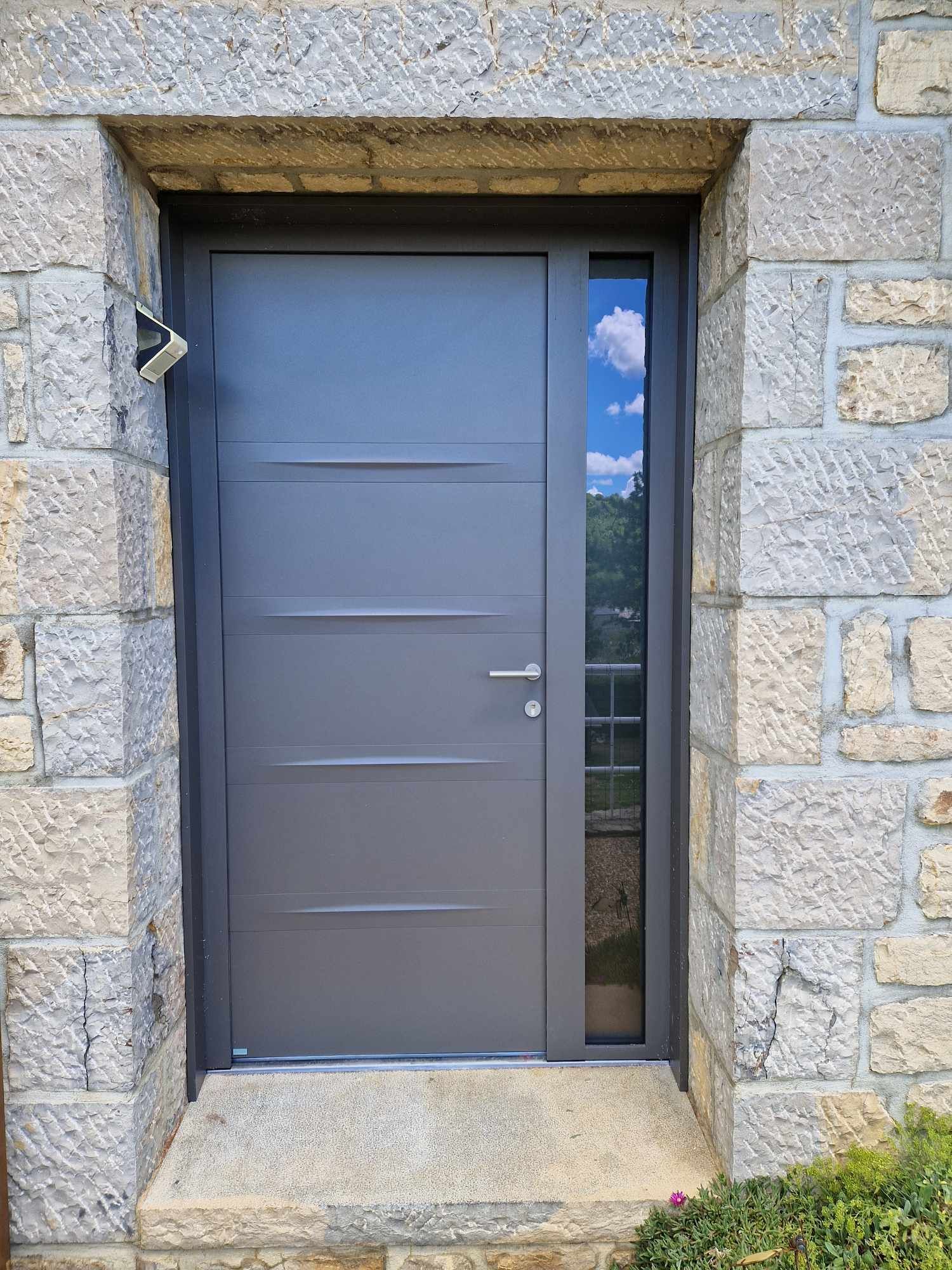 Porte d'entrée grise avec une fenêtre sur le côté.