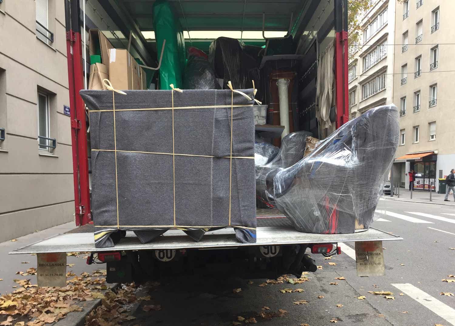 Un camion décharge des marchandises emballées et empilées dans une rue de la ville, sous l'auvent d'un bâtiment.