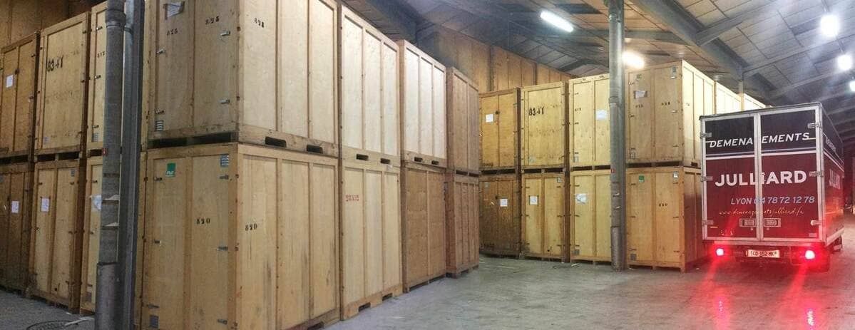 Des caisses d'expédition en bois empilées dans un entrepôt, avec un chariot élévateur et des feux rouges sur la droite.