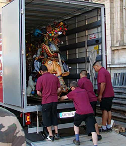 Des personnes déchargent une grande sculpture colorée d'un camion devant un bâtiment