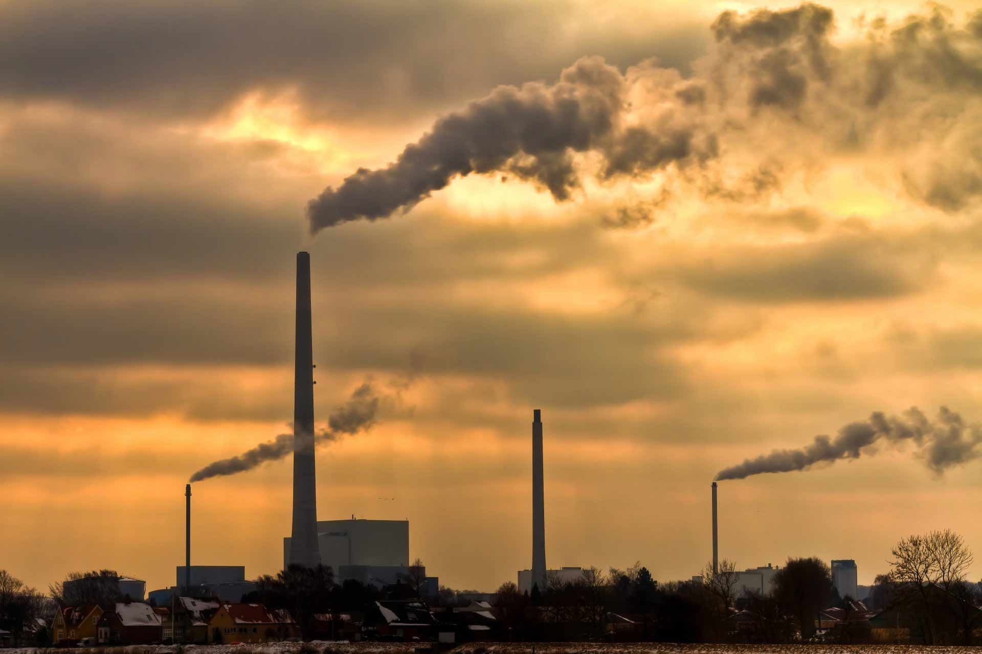 Cheminées industrielles crachant une fumée noire au coucher du soleil sur un horizon industriel