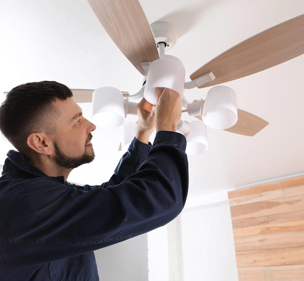 Un hombre instala un ventilador de techo con aspas de madera en una habitación luminosa.