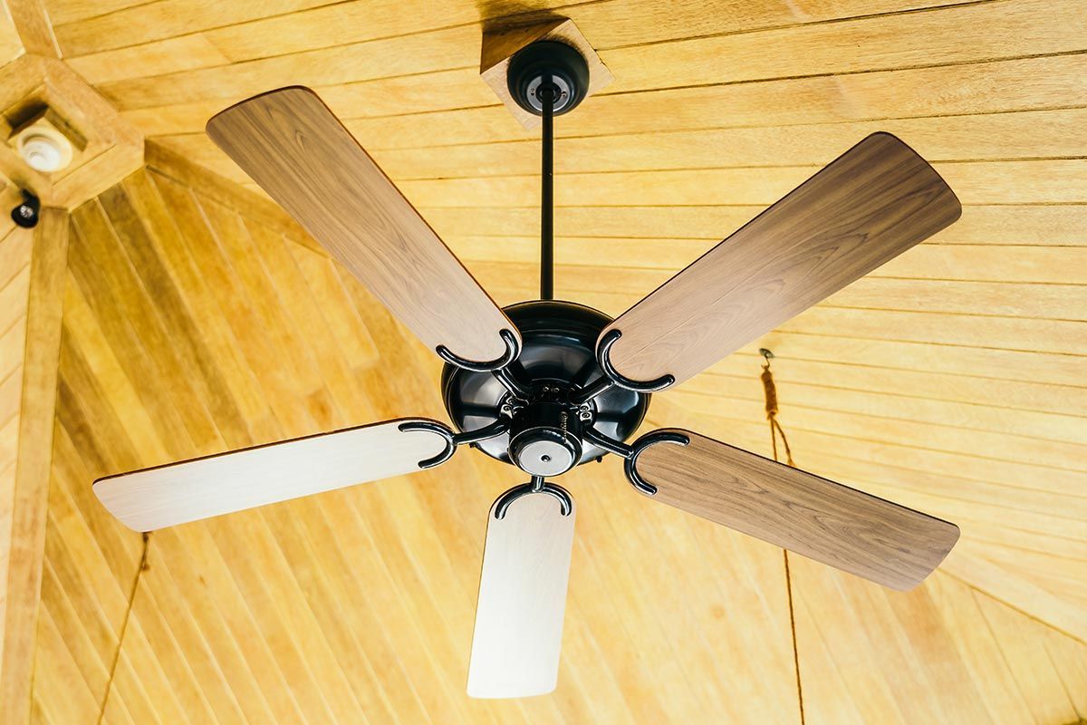 Ventilador de techo con cinco aspas de madera sobre un techo revestido de paneles de madera clara.
