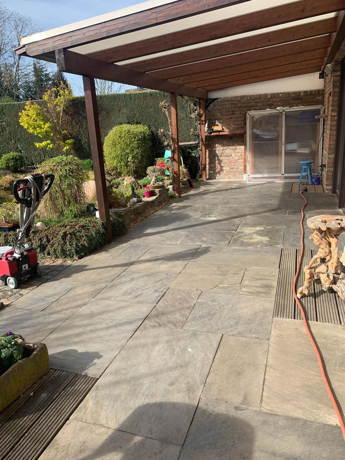 Eine Terrasse mit Pergola und Rasenmäher vor einem Haus.
