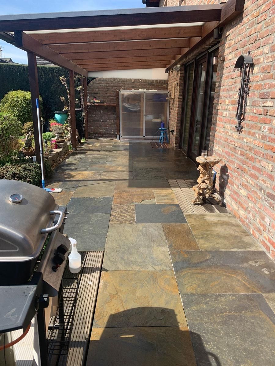 Auf einer Terrasse neben einer Backsteinmauer steht ein Grill.