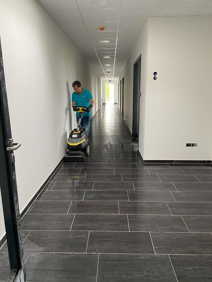 Ein Mann reinigt mit einem Staubsauger den Boden eines Flurs.