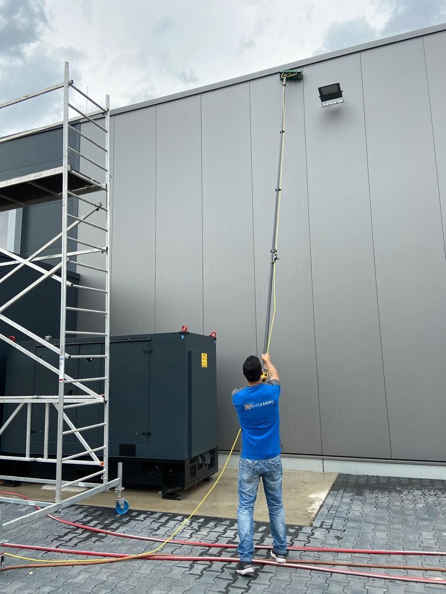 Ein Mann reinigt die Seite eines Gebäudes mit einer langen Stange.