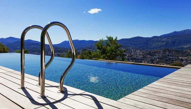 Piscina infinita con vistas a las montañas y a una ciudad, con un cielo azul brillante.
