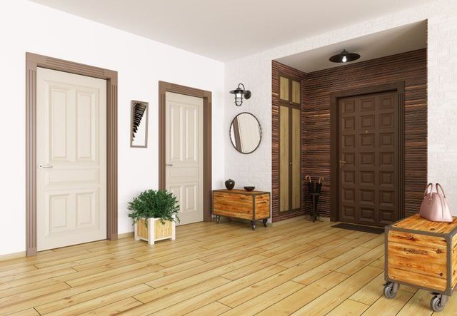 Recibidor con suelo de madera, tres puertas y muebles de madera; uno de ellos con espejo y elementos decorativos.
