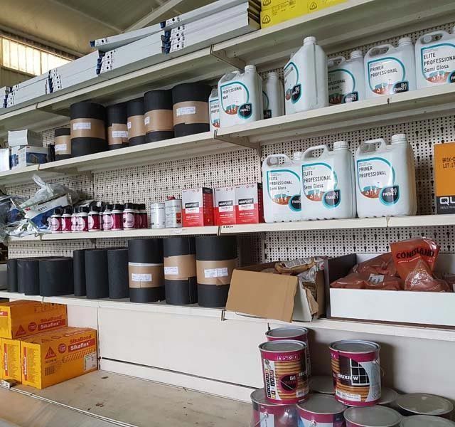 Estantes llenos de materiales de construcción, incluidos rollos de material negro, latas y contenedores de plástico blanco.