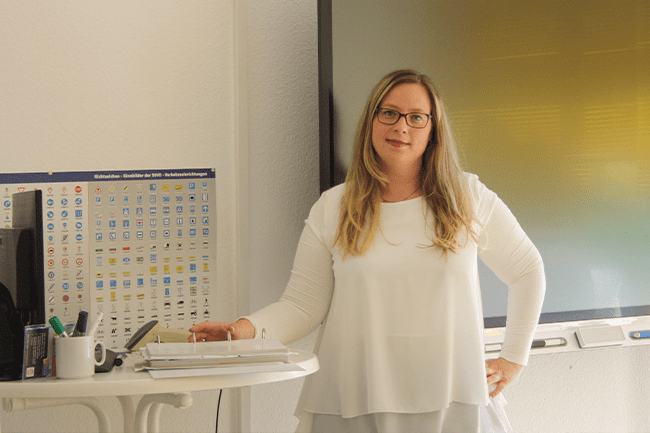 Eine Frau im weißen Hemd steht vor einem großen Bildschirm