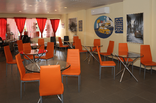 Ein Raum mit orangefarbenen Stühlen und Tischen mit einem Gemälde eines Taxis an der Wand