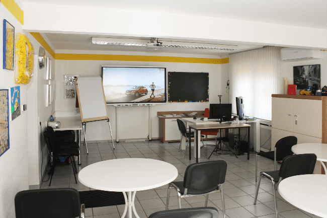 Ein Raum mit Tischen und Stühlen und einem großen Bildschirm an der Wand