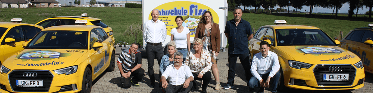 Team der Fahrschule vor Fahrzeugen