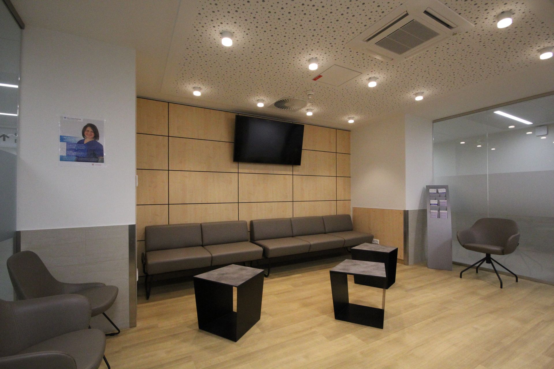 Ein Wartezimmer mit Stühlen, Tischen und einem Flachbildfernseher.