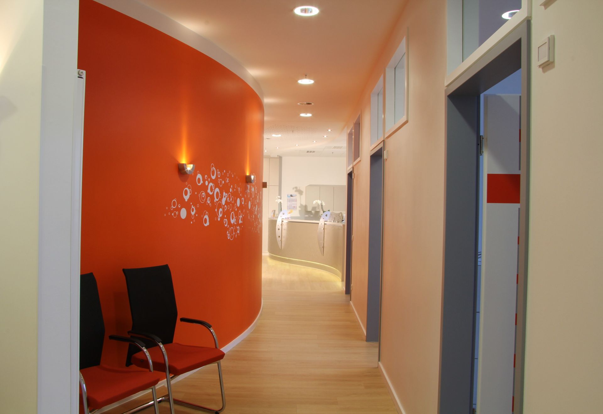 Ein langer Flur mit orangefarbenen Wänden und Stühlen darin