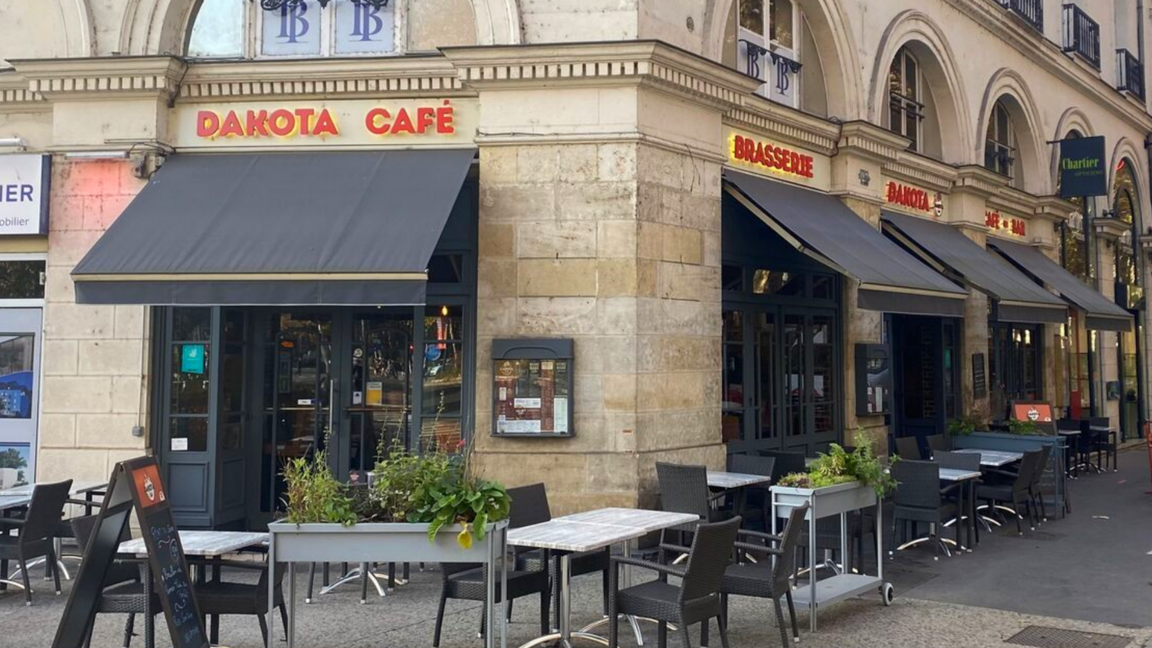 Façade du Dakota Cafe avec terrasse couverte d'auvents noirs, dans une rue de la ville.