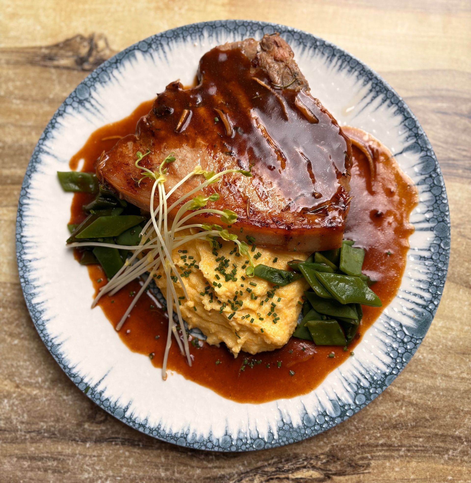 Filet de porc en sauce, servi sur une purée de patates douces et des haricots verts dans une assiette à motifs.