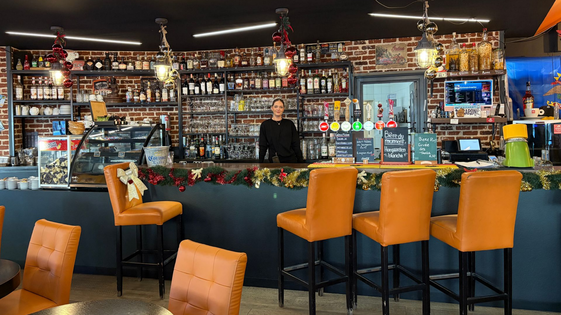 Intérieur du Dakota Café, des tabourets orange et des étagères remplies de bouteilles.