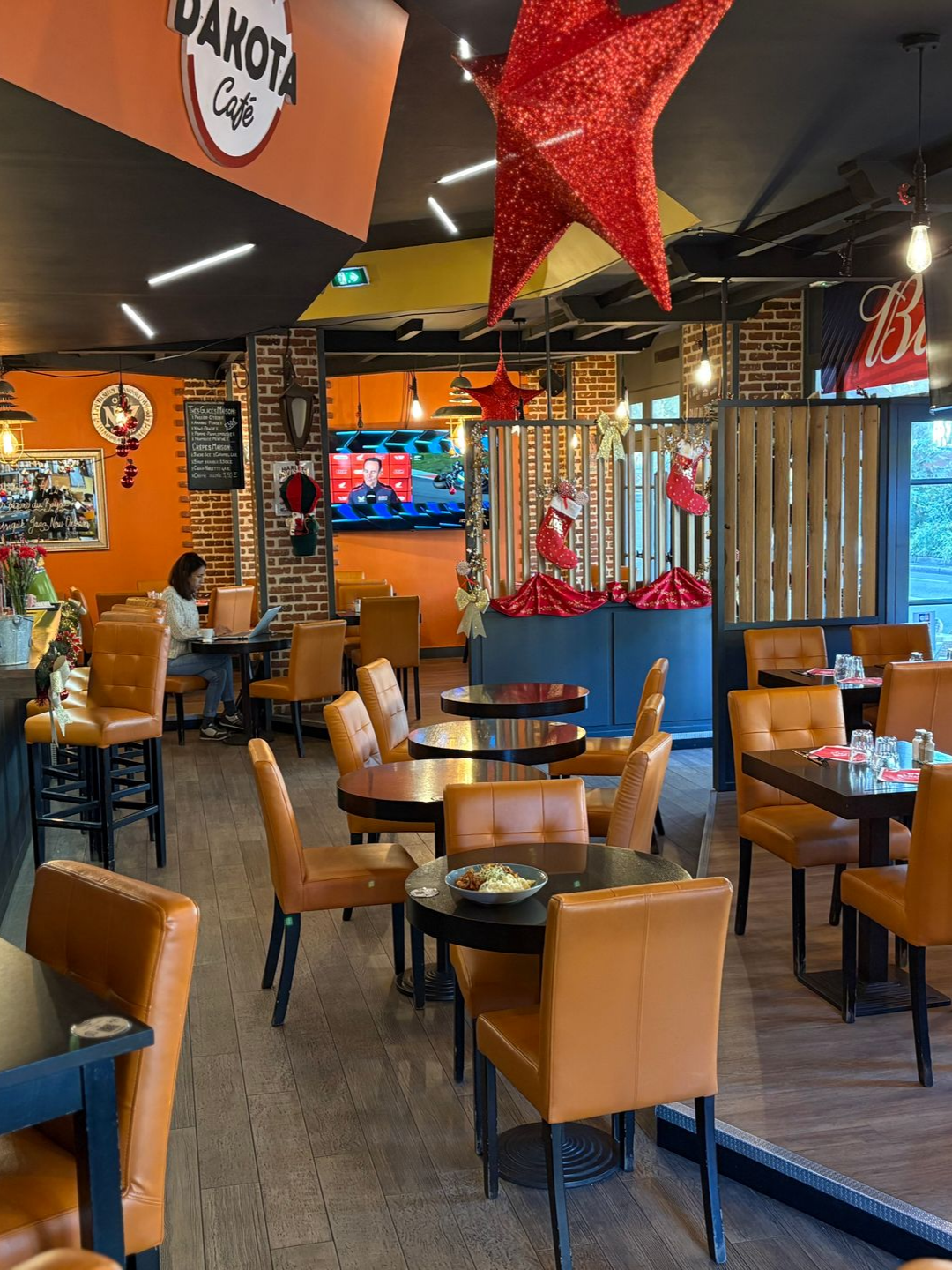 Intérieur du Dakota Cafe, décor orange et marron, tables, chaises et quelques clients. Décorations de Noël.