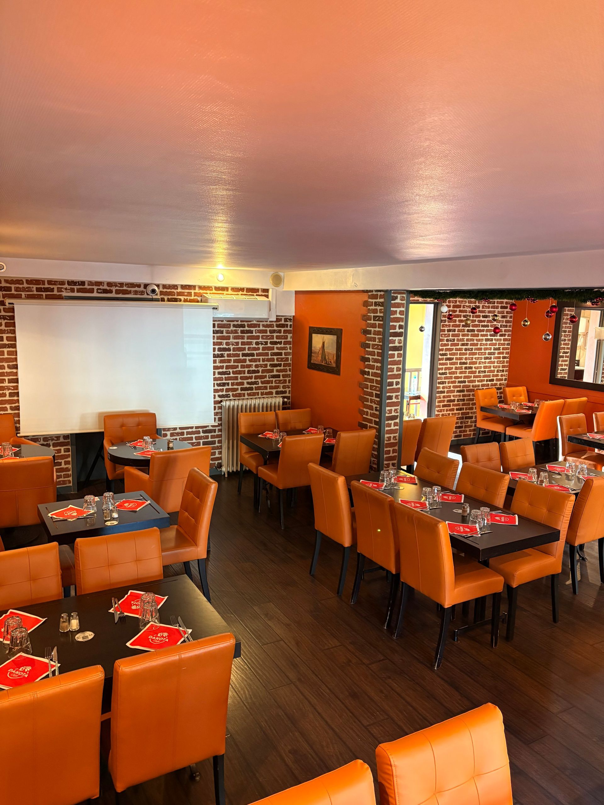 Intérieur de restaurant avec chaises orange, les tables sombres, les murs en briques et un paravent blanc.